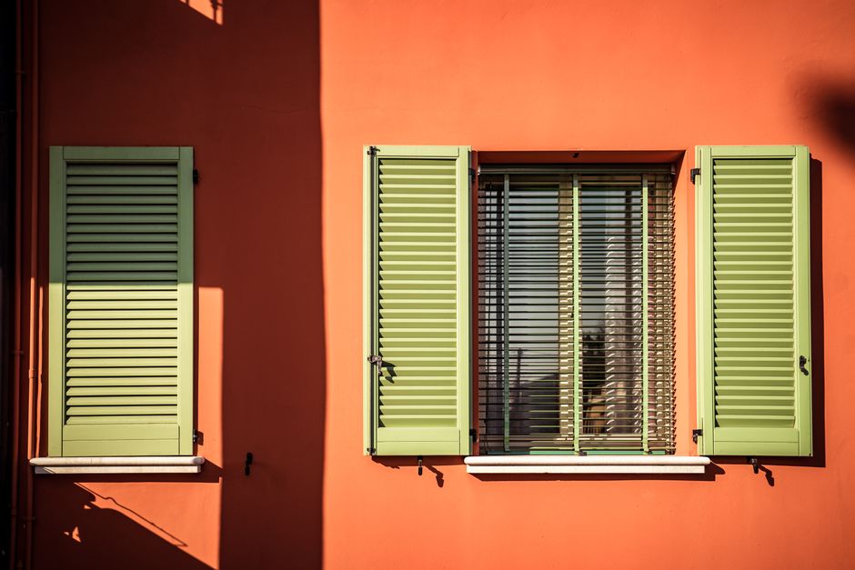 An exterior with green shutters against an orange painted wall.